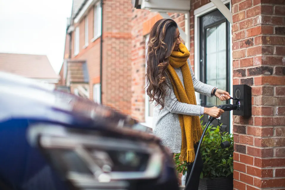 A driver connecting a wall-mounted charger outside a home